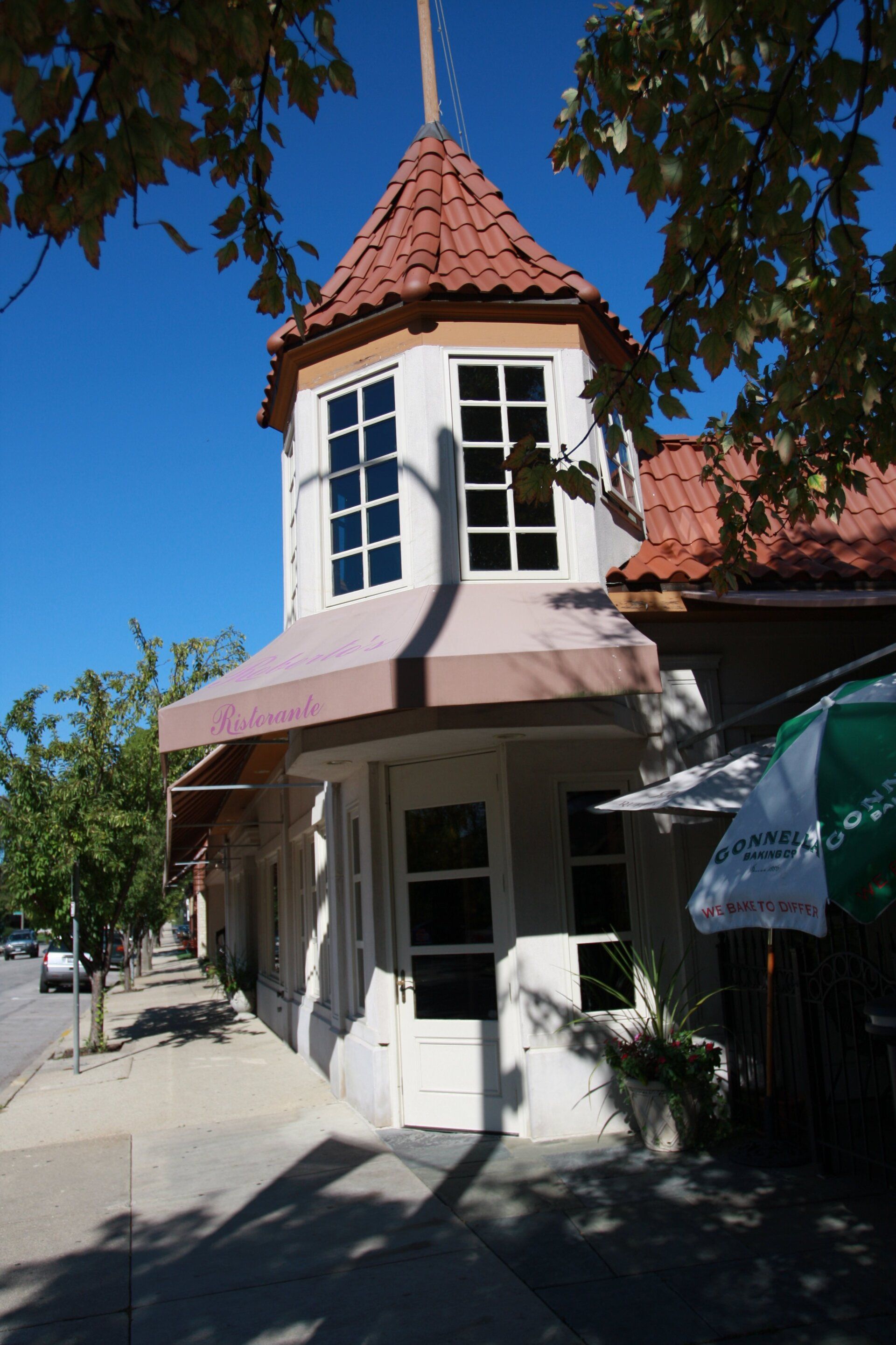 A white building with a red roof and a pink awning