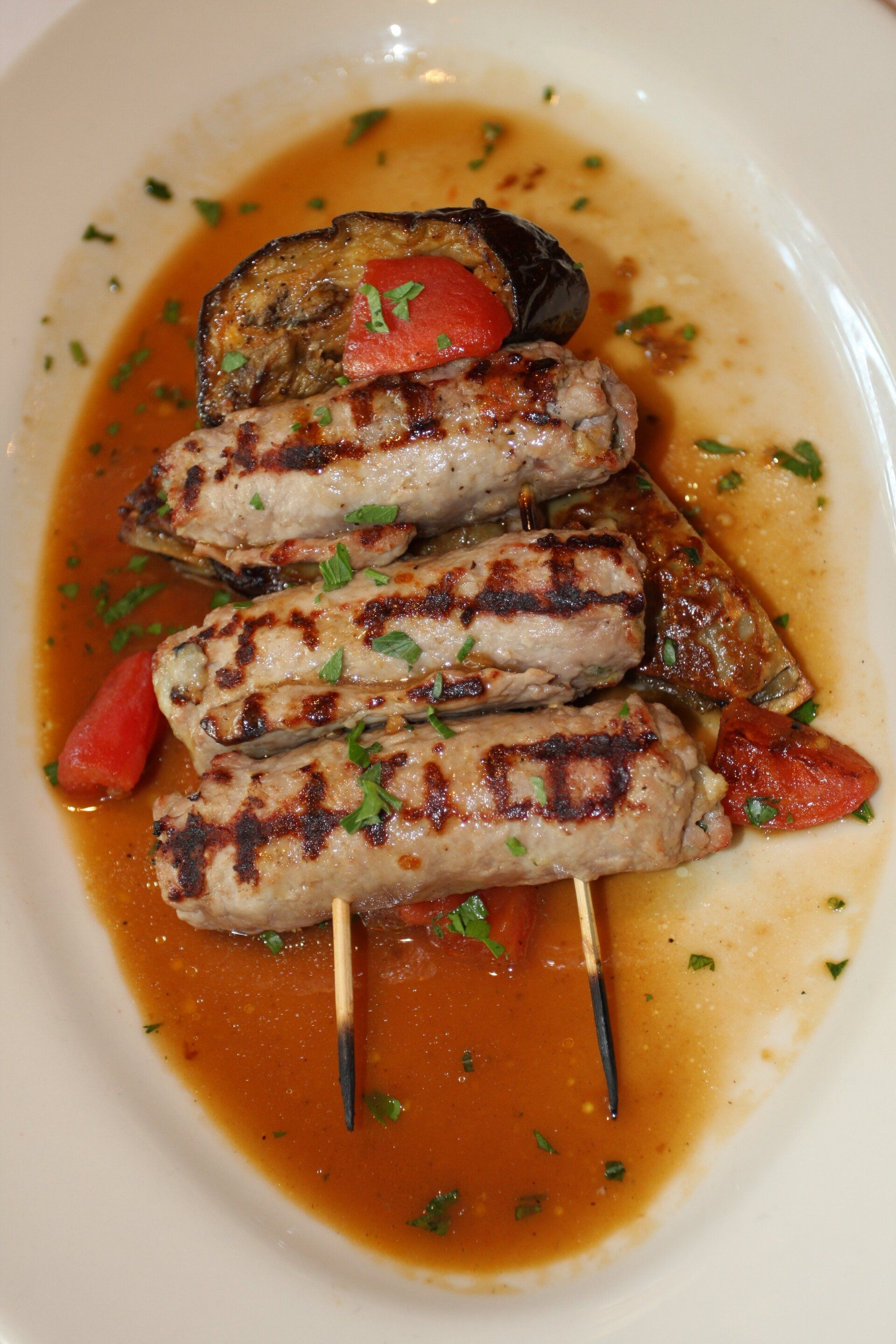 A white plate topped with grilled sausages and vegetables.
