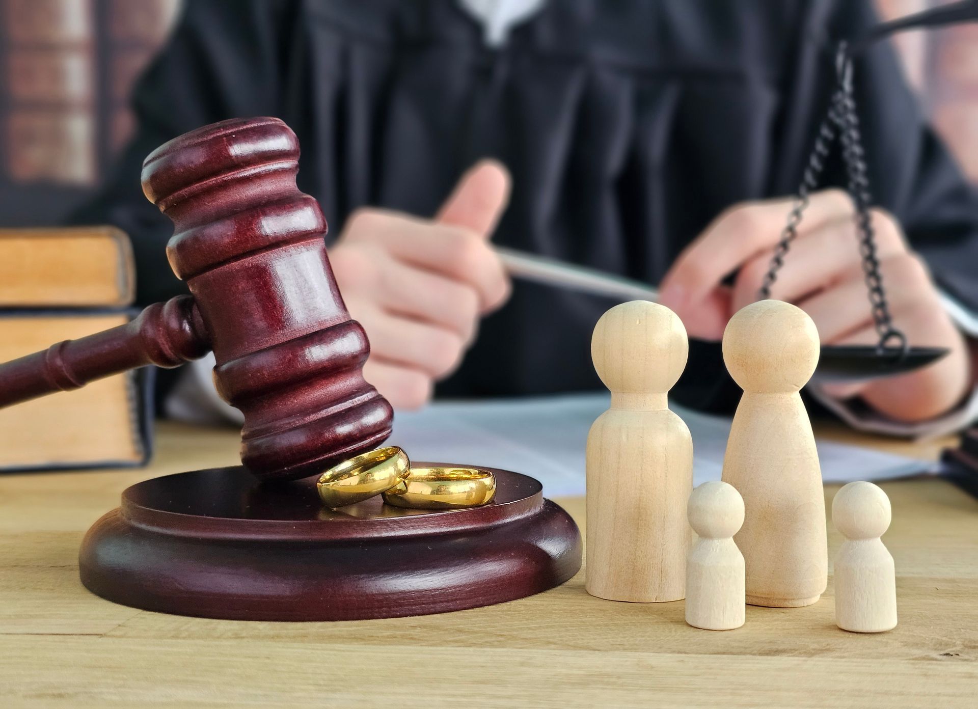 A wooden gavel and wedding rings sit before a judge and four wooden figures representing a family on a desk.