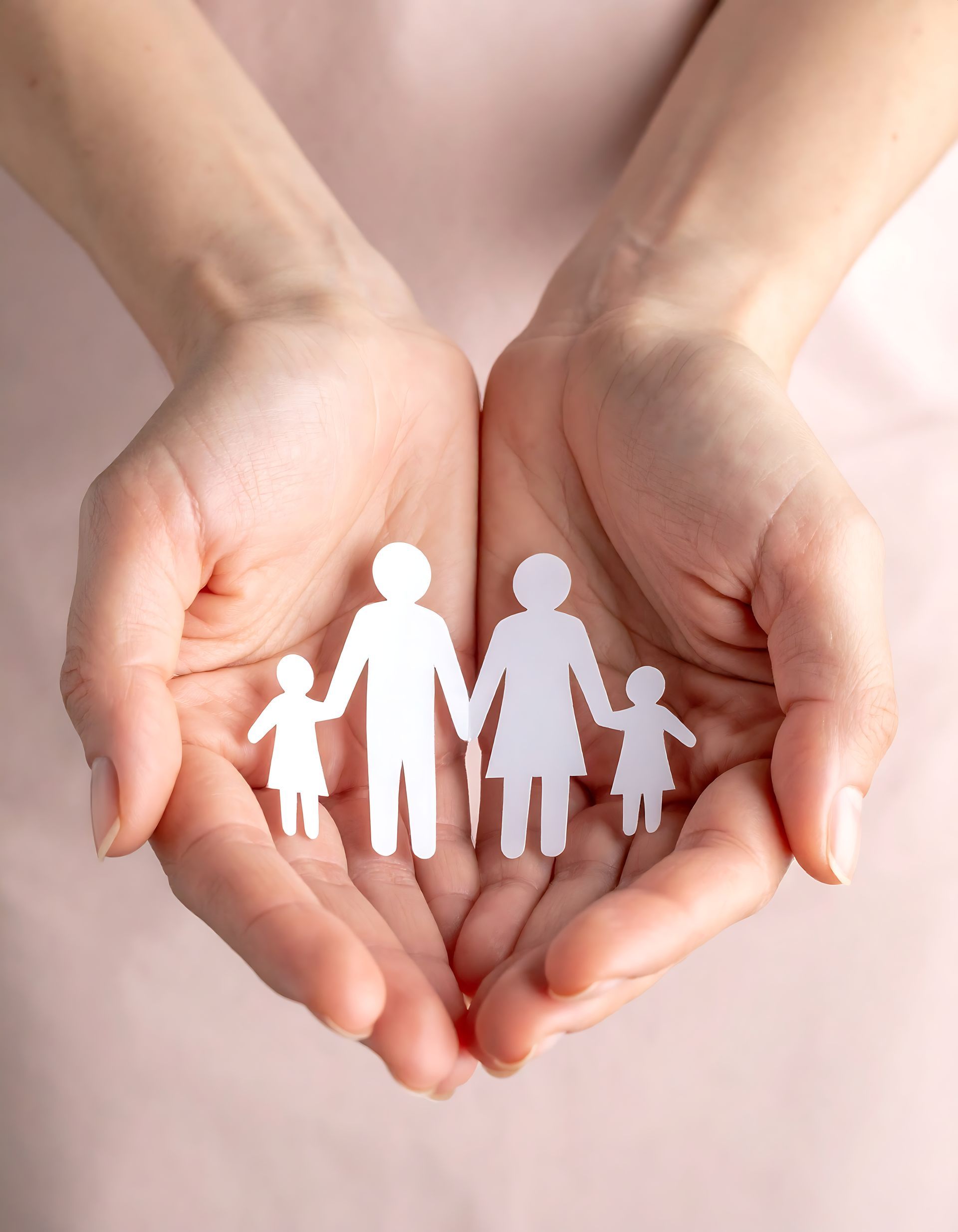 A person's cupped hands holding a small, white paper cutout of a family consisting of two adults and two children.