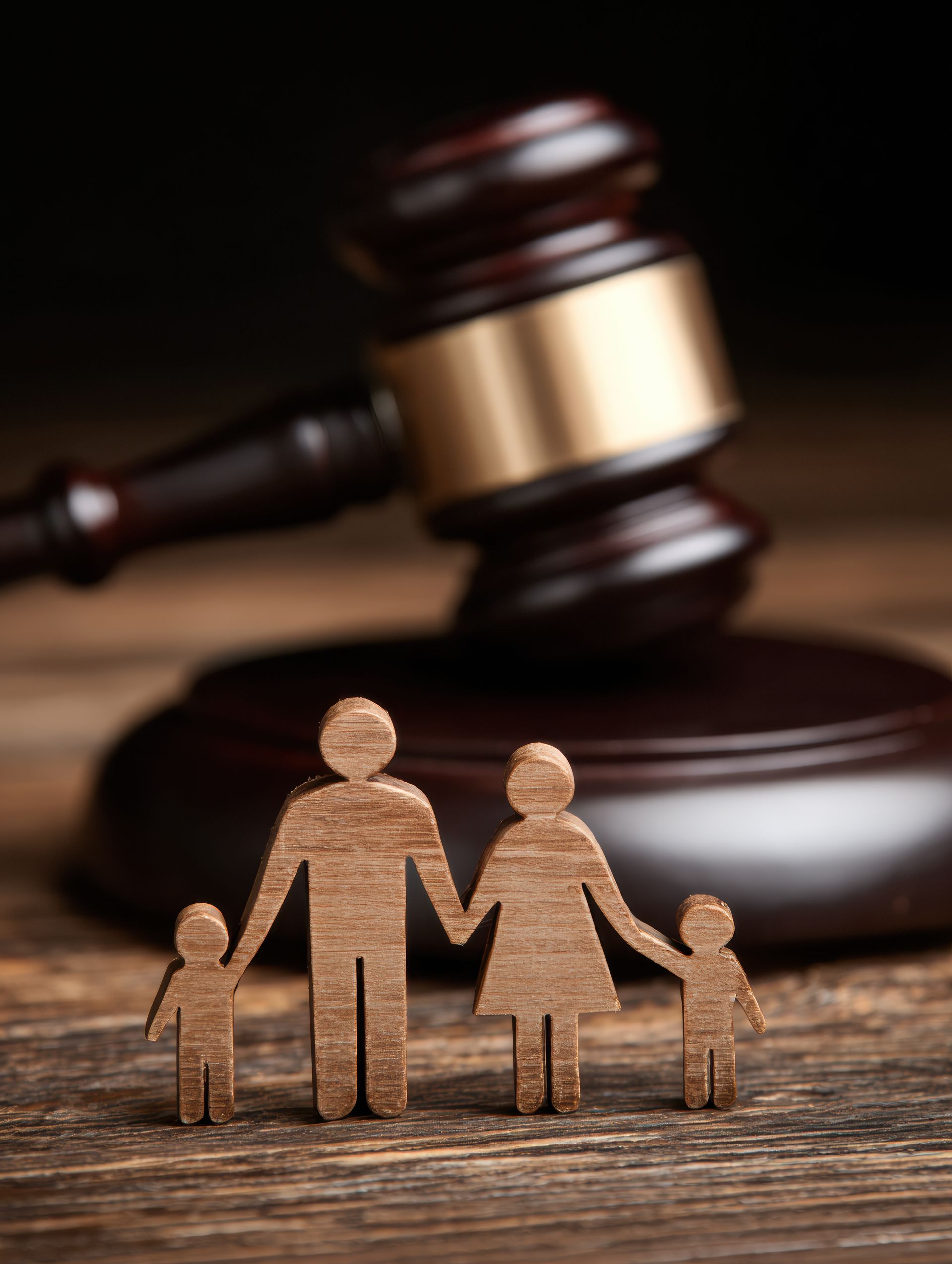 A wooden family figurine stands in front of a judge's gavel on a wooden surface, representing family law. A wooden family figurine stands in front of a judge's gavel on a wooden surface, representing family law.