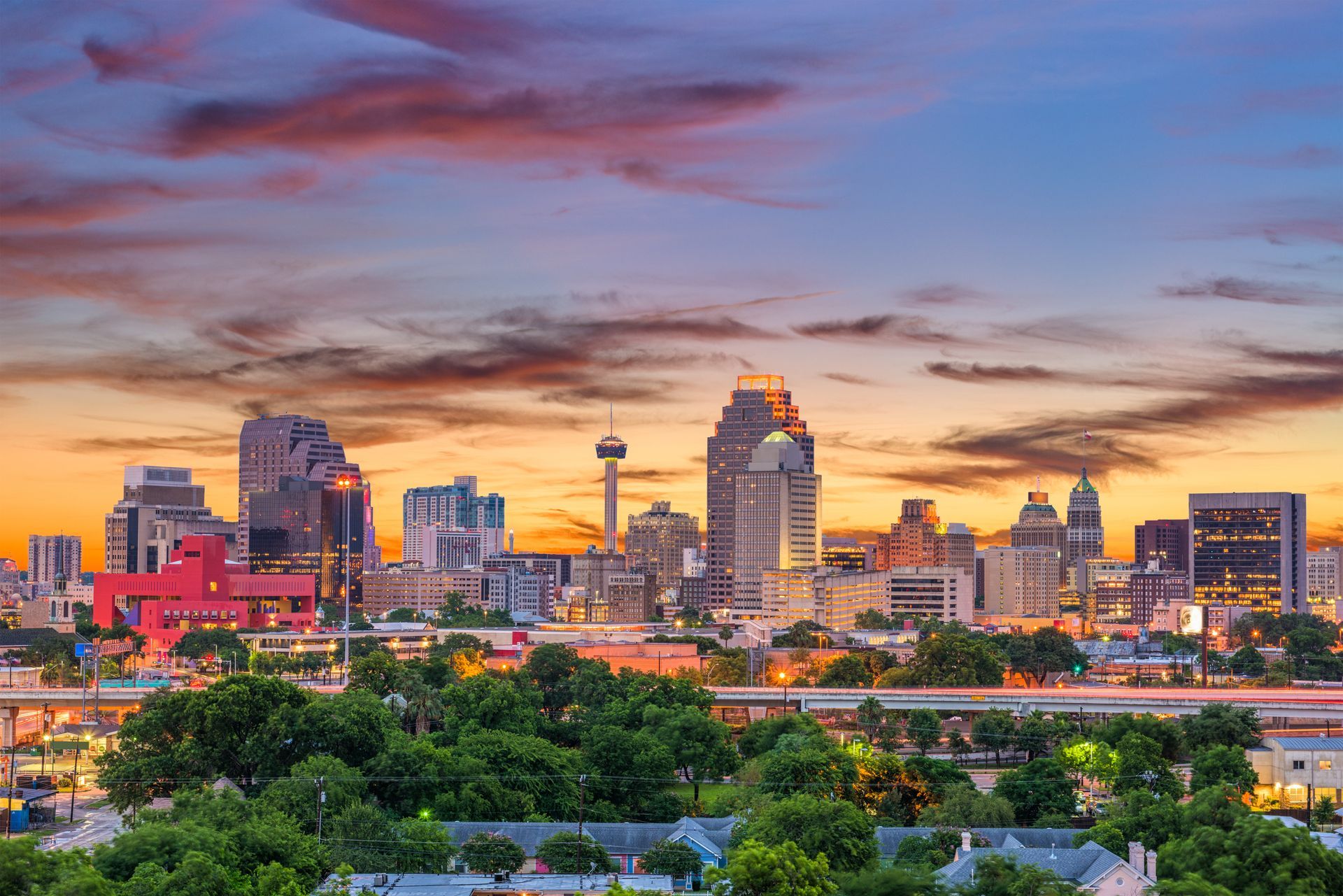 San Antonio skyline at sunset, featuring the Tower of the Americas amidst downtown buildings under a colorful sky.