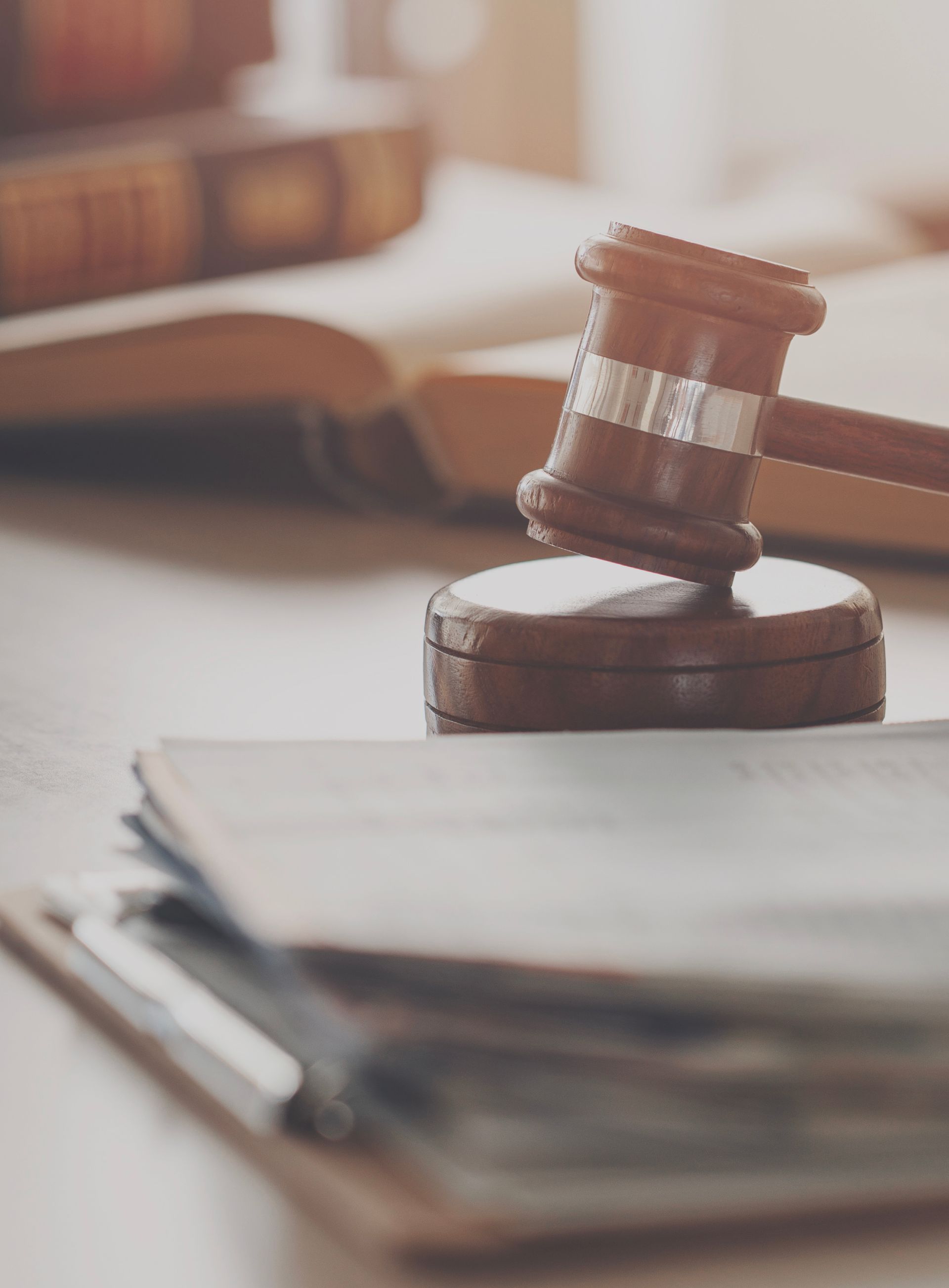 A wooden judge's gavel rests on its block next to legal documents and an open book on a desk.