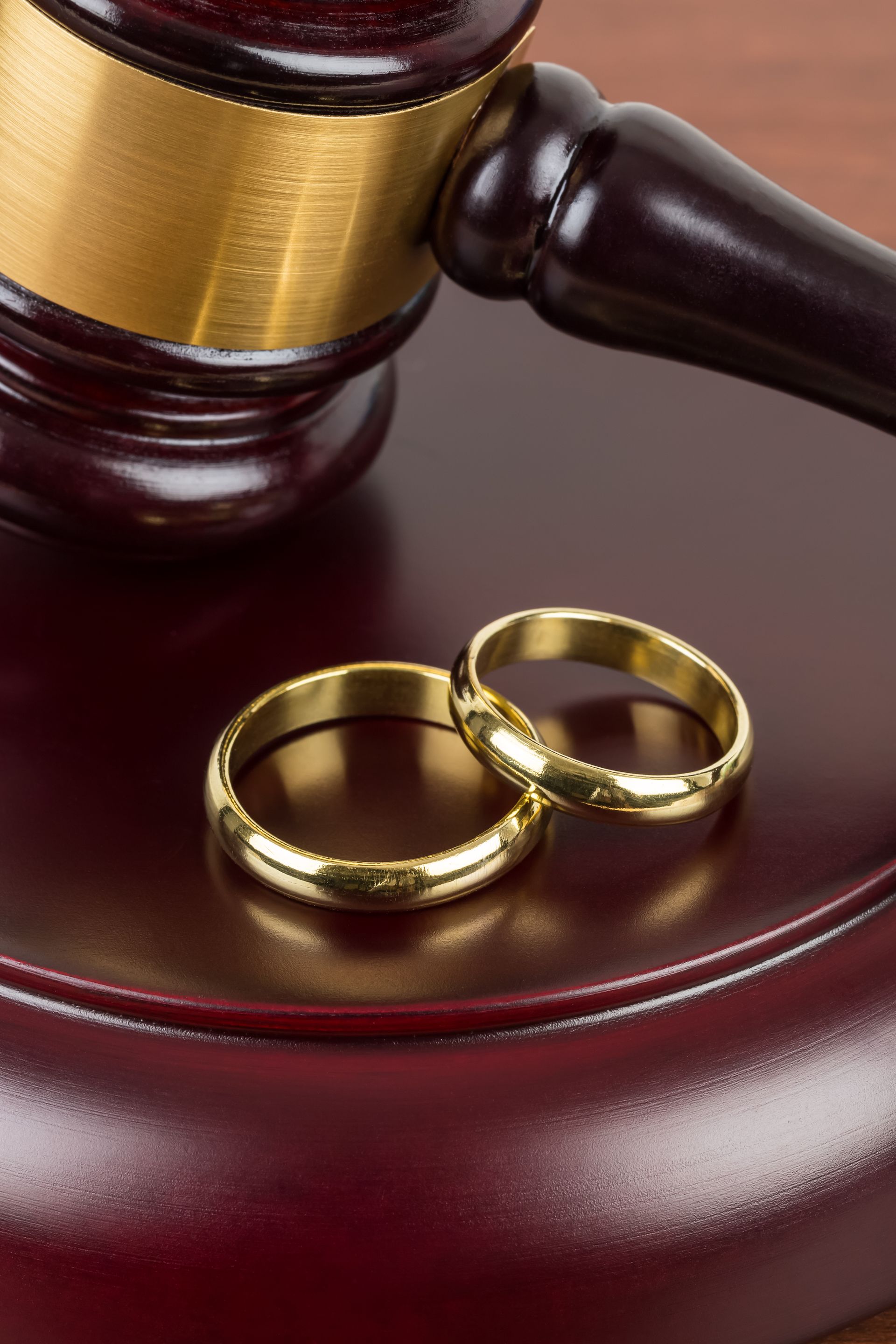 A wooden gavel rests on a base next to two gold wedding rings, symbolizing a legal divorce proceeding. A wooden gavel rests on a base next to two gold wedding rings, symbolizing a legal divorce proceeding.