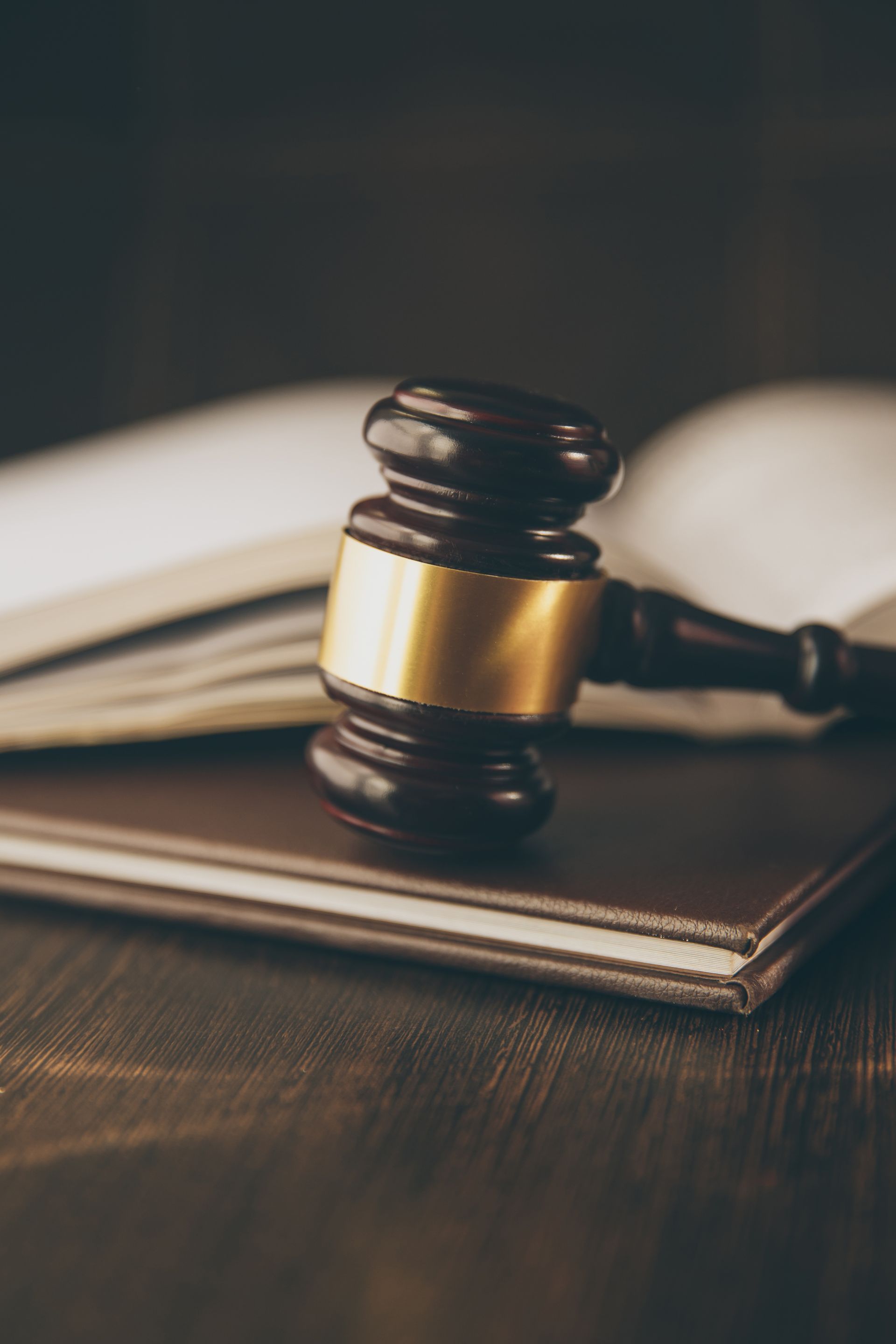 A dark wooden gavel with a gold band rests on top of a closed book on a dark wooden surface.
