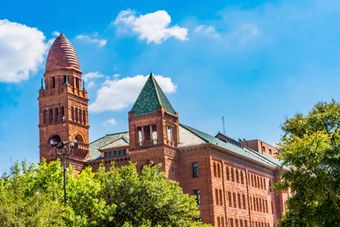 A historic red brick building with a tall, domed tower and green shingled roofs under a bright blue sky with clouds. A historic red brick building with a tall, domed tower and green shingled roofs under a bright blue sky with clouds.