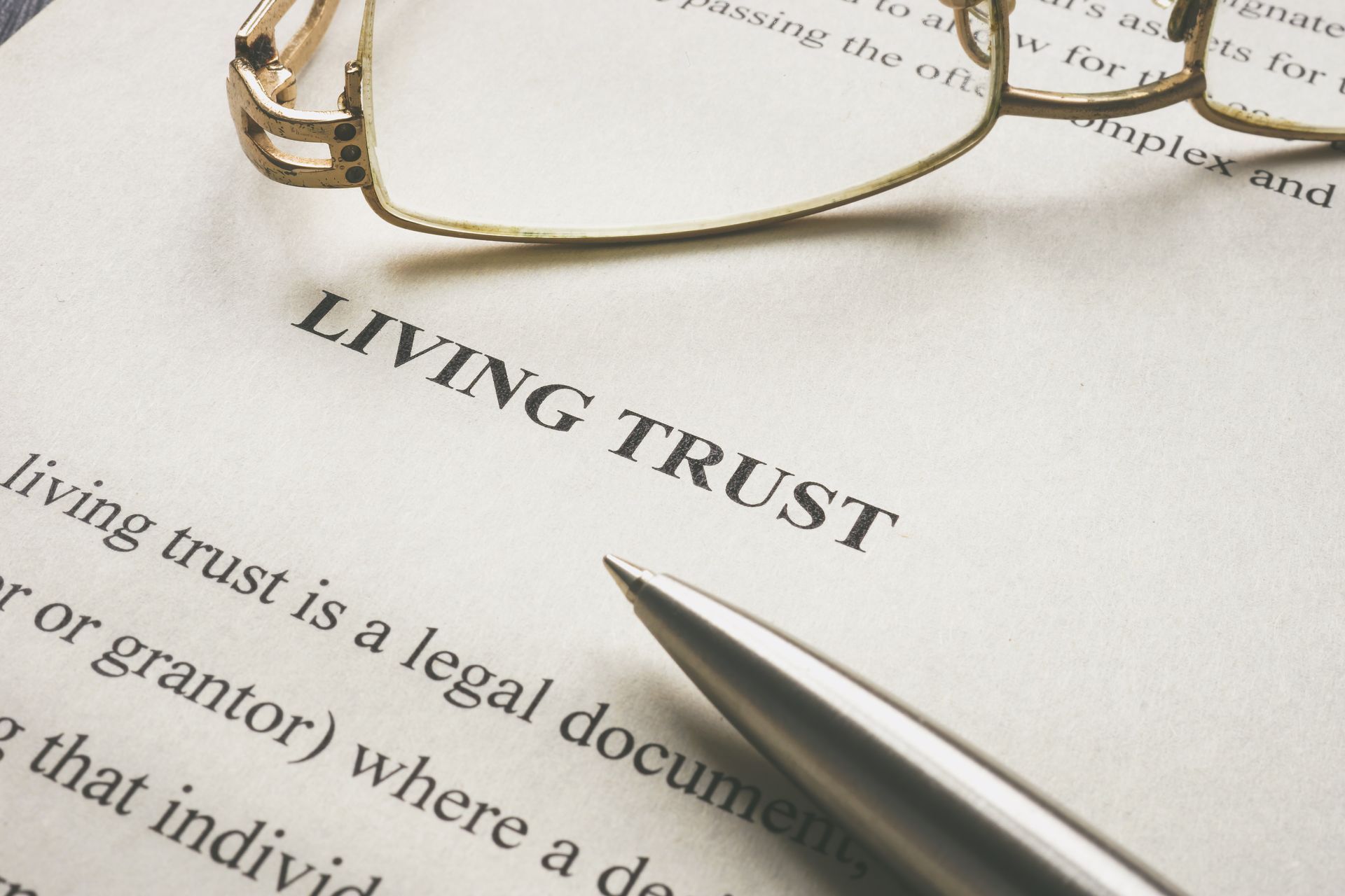 A silver pen and eyeglasses resting on a document titled LIVING TRUST. A silver pen and eyeglasses resting on a document titled LIVING TRUST.