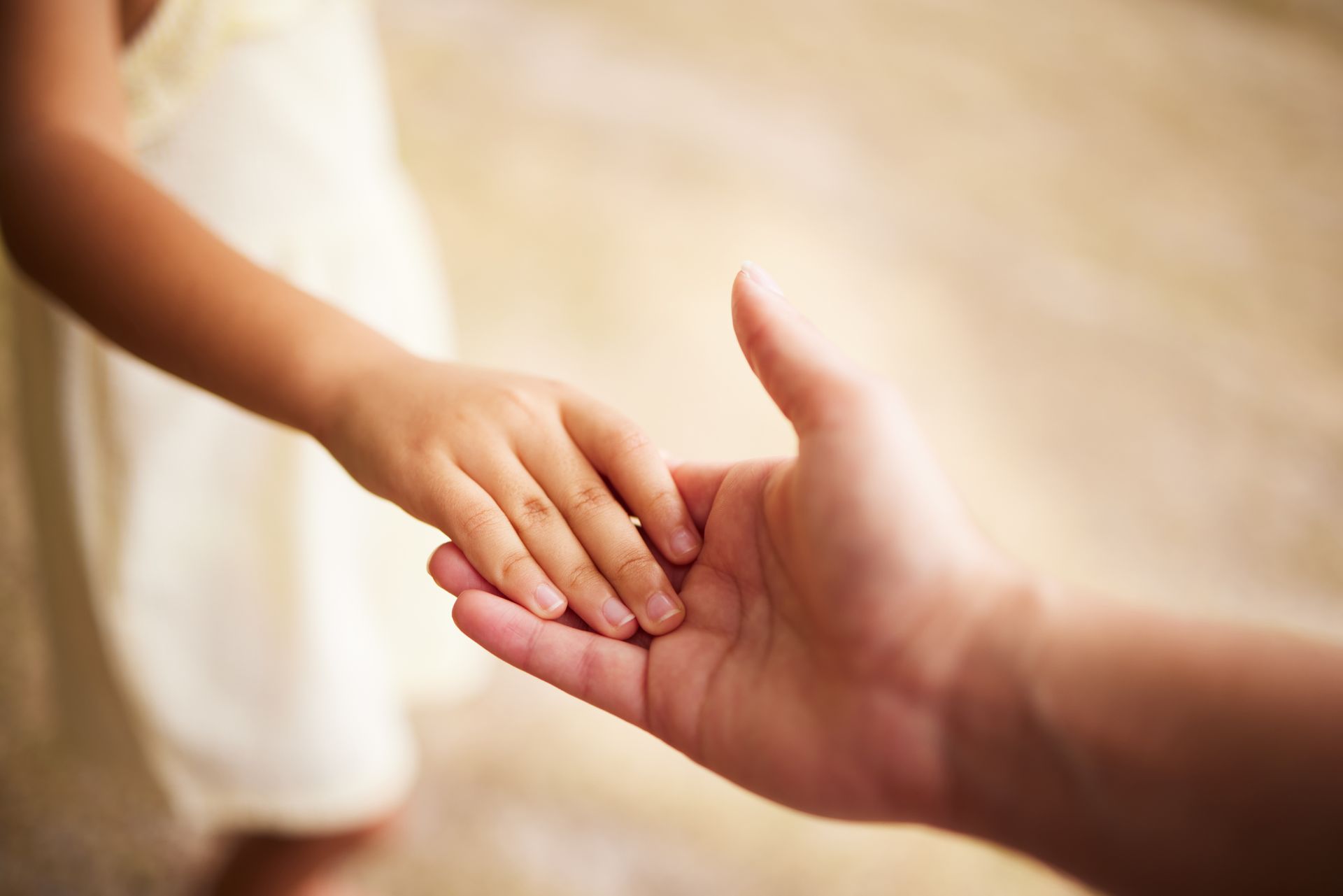 A small hand reaches out to touch an open adult hand against a softly blurred background.