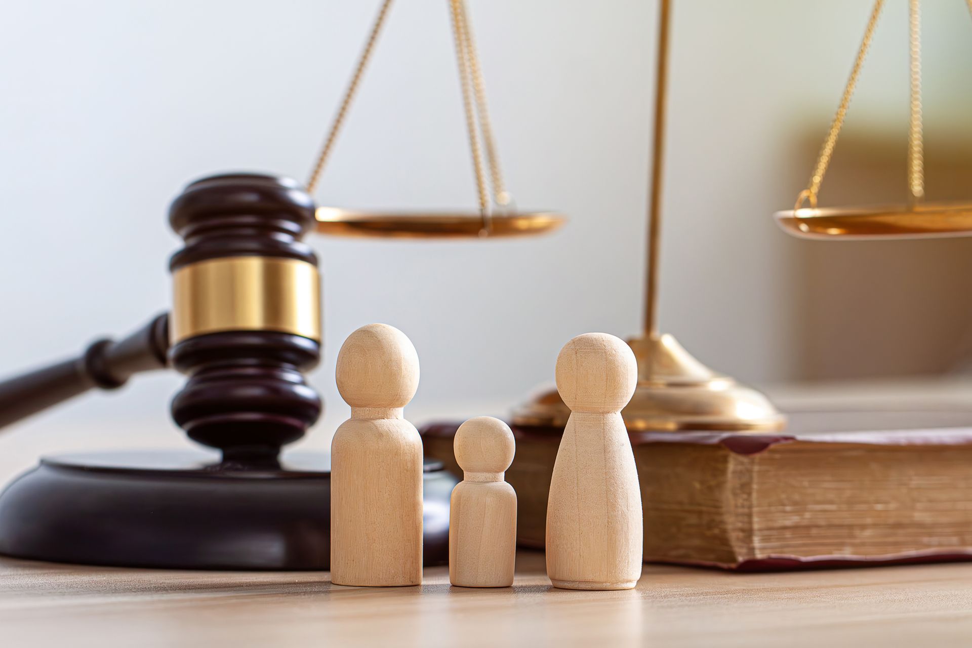 A judge's gavel, scales of justice, and a legal book placed behind three small wooden figures on a desk.