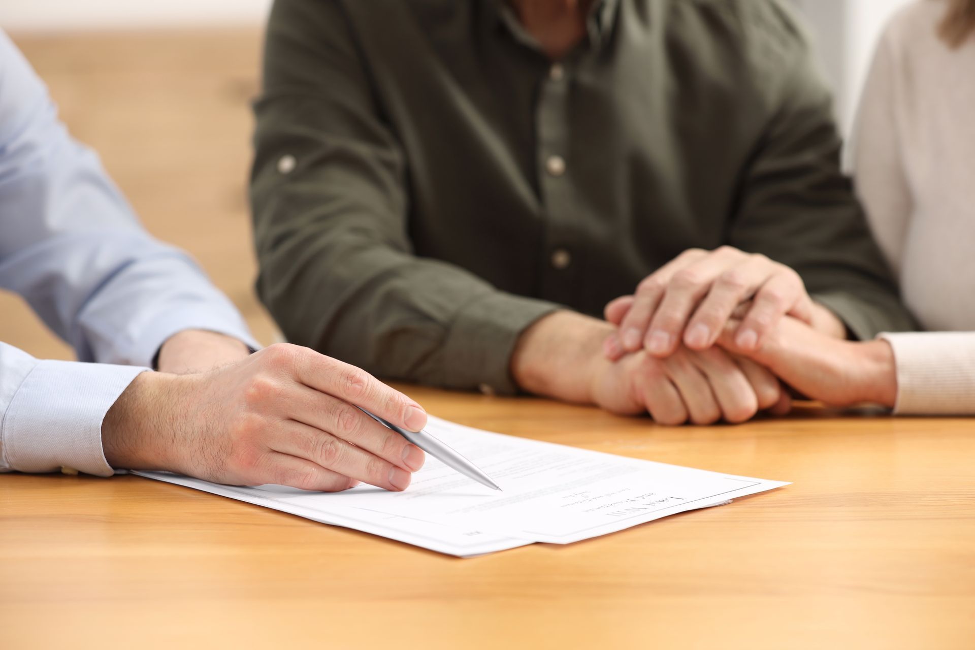 A professional points to a document on a wooden table, while two people hold hands in the background.