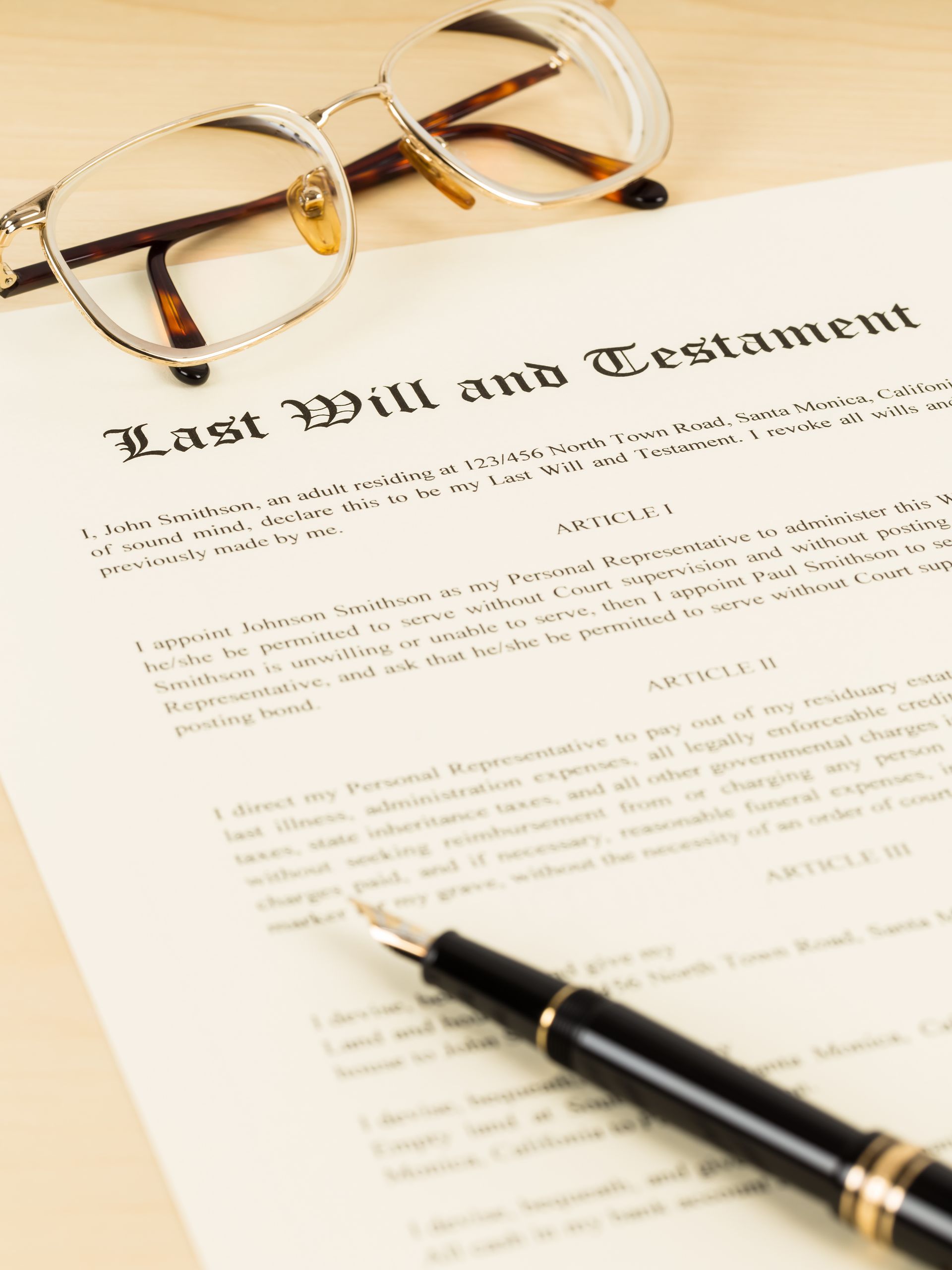 A pair of eyeglasses and a black fountain pen resting on a document titled Last Will and Testament.