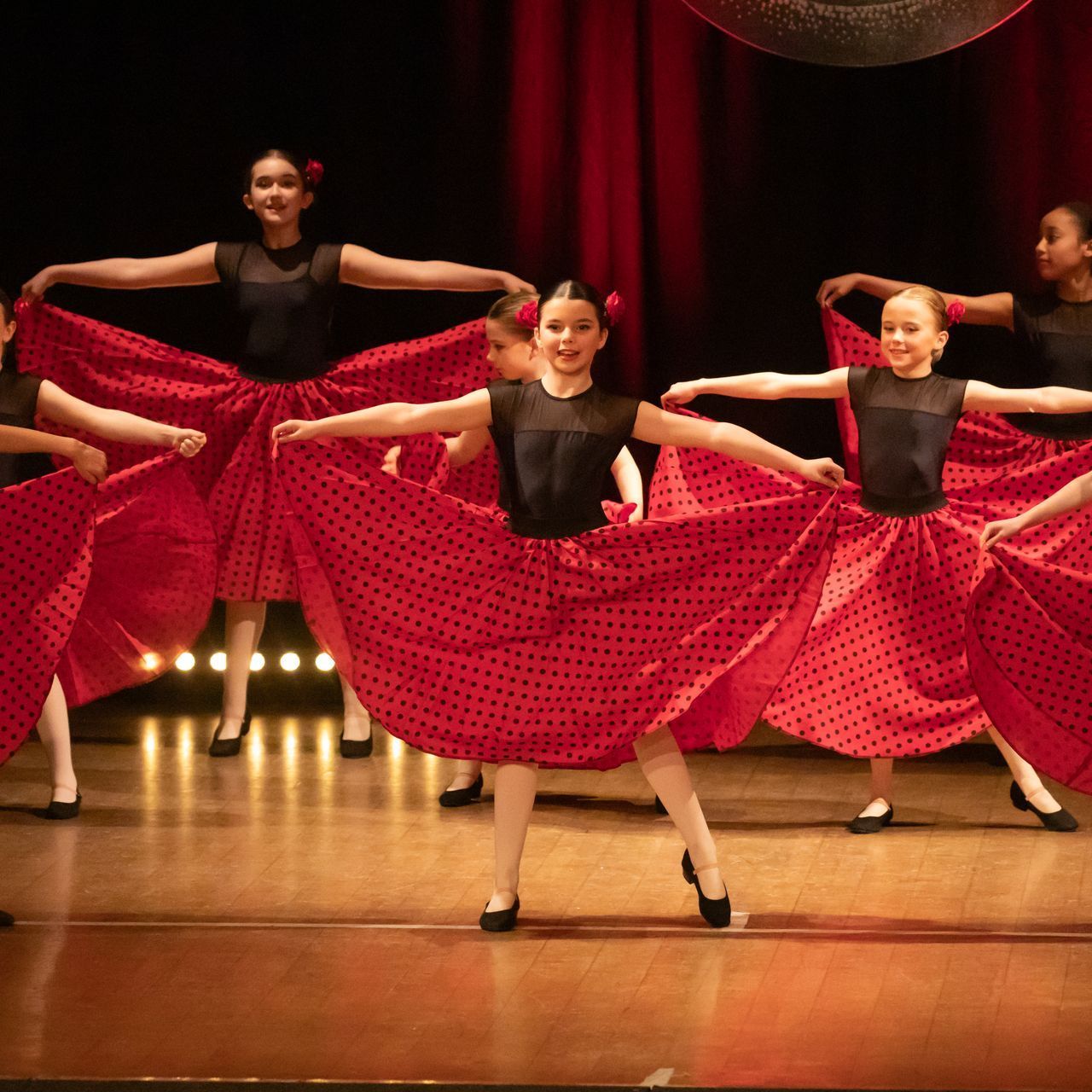 A group of girls in red polka dot skirts are dancing on a stage