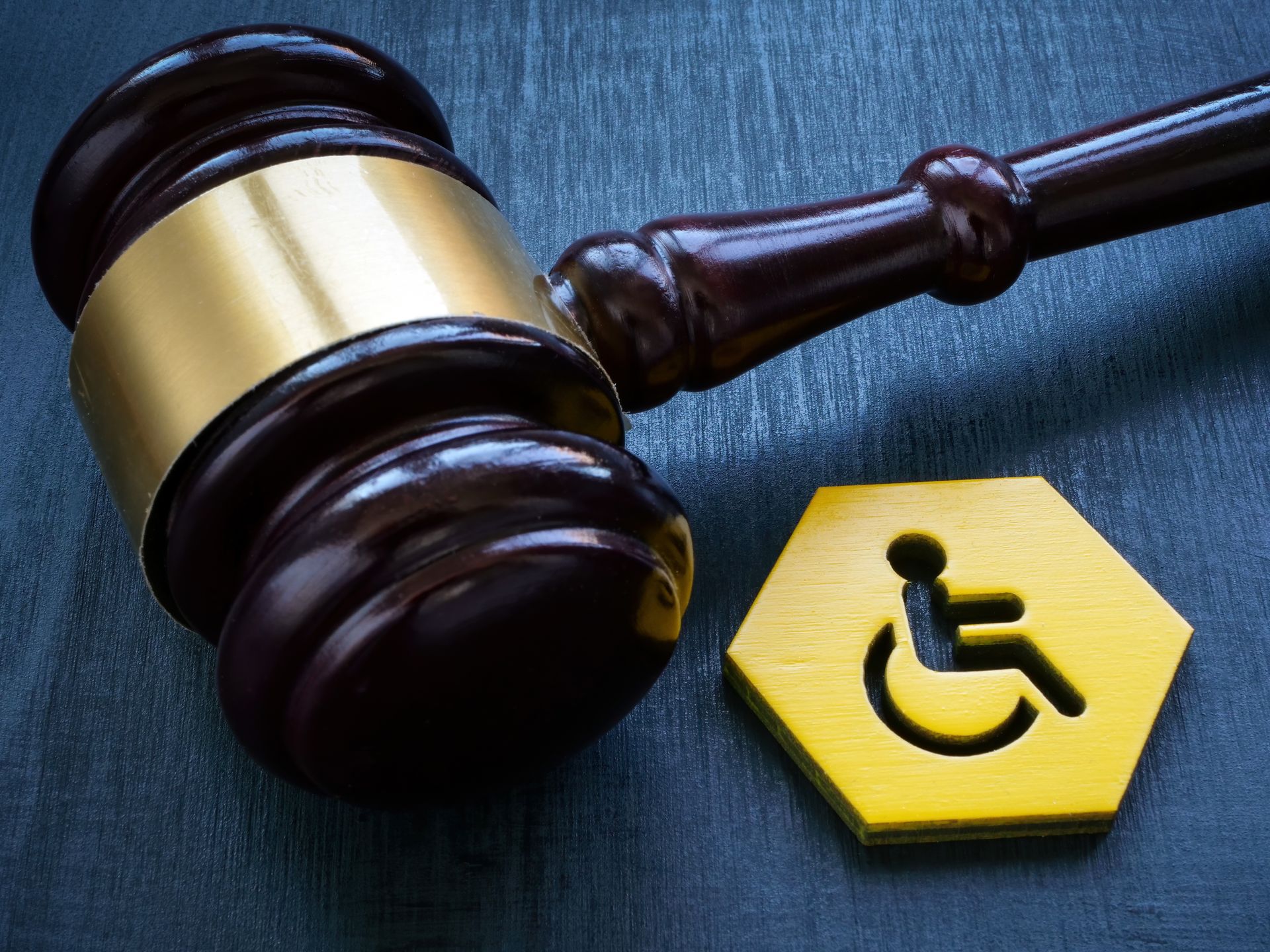 A judge’s gavel lies beside a yellow disability access symbol on a dark surface.