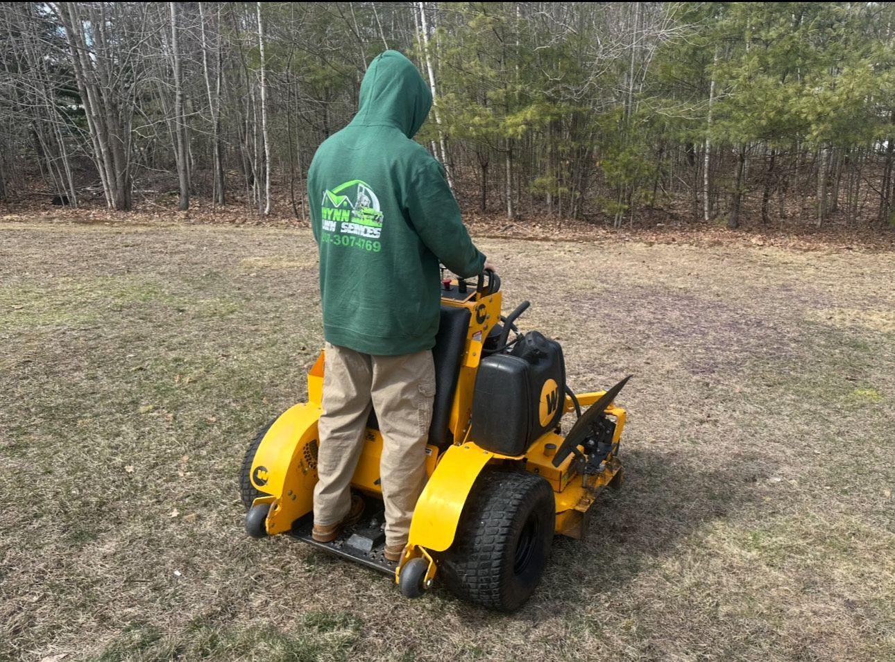 A man in a green hoodie is riding a yellow lawn mower.