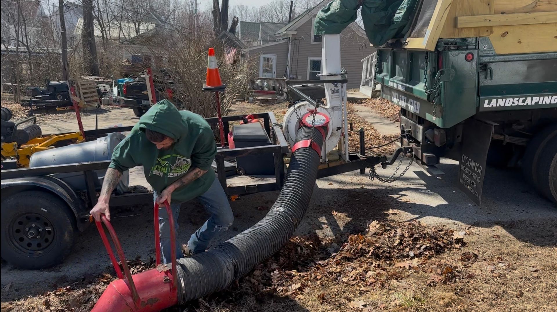 A man is working on a hose next to a dump truck.