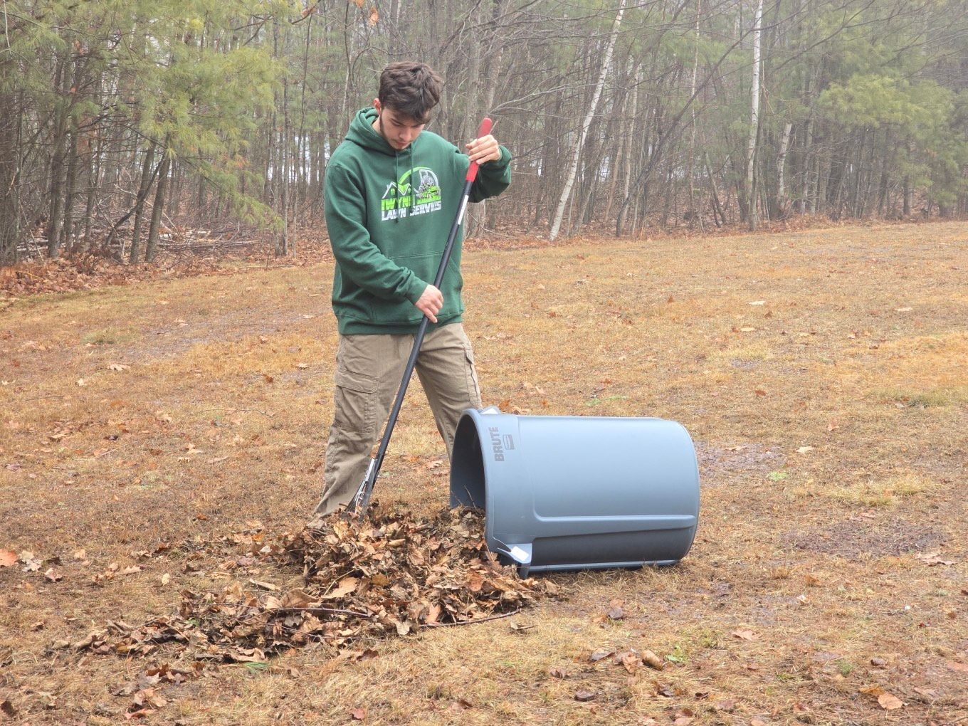 A man in a green hoodie is raking leaves in a field.