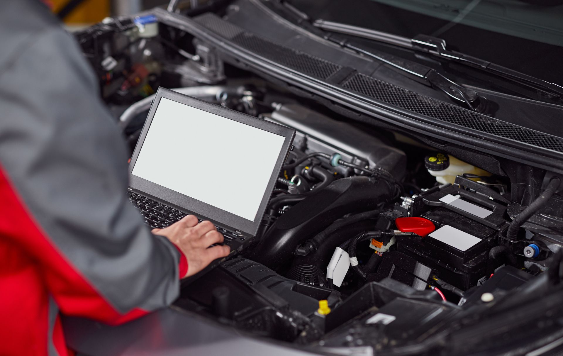 A mechanic is using a laptop computer to check the engine of a car.