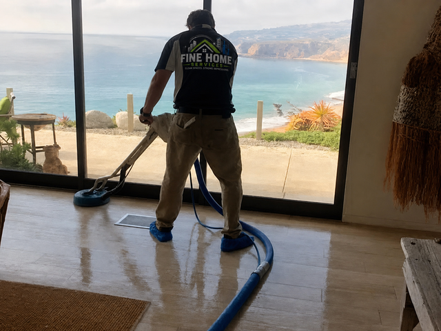Person vacuuming a seaside room, with ocean visible through open doors.