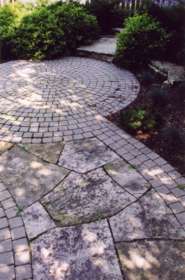 A landscaped garden featuring a circular cobblestone patio connected to a pathway of large, irregular flagstone pavers.