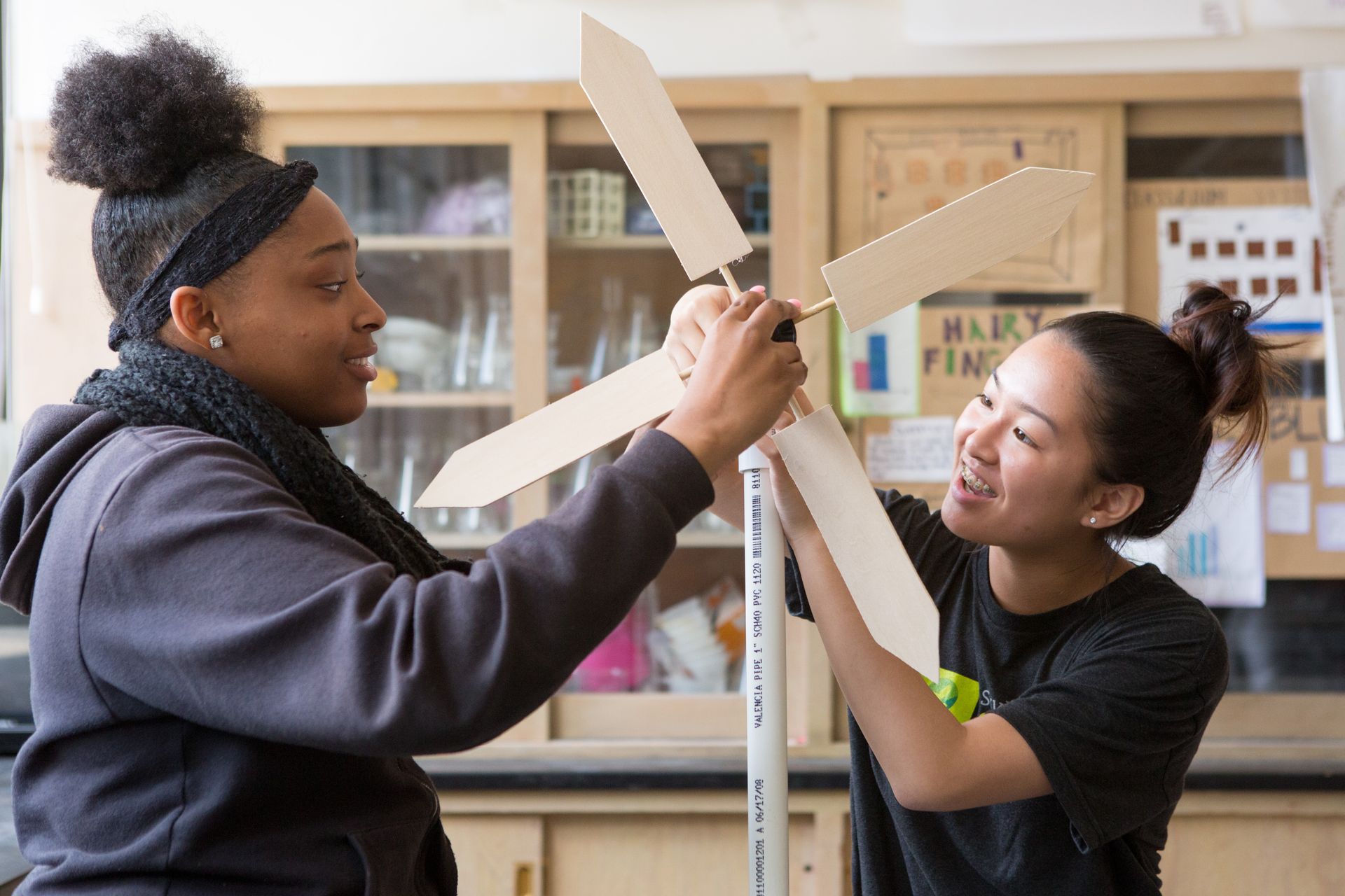 Two young women are working on a wooden windmill in a lab.