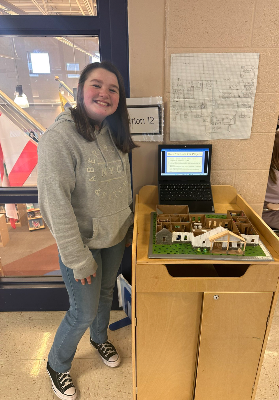 A girl is standing next to a model of a house.