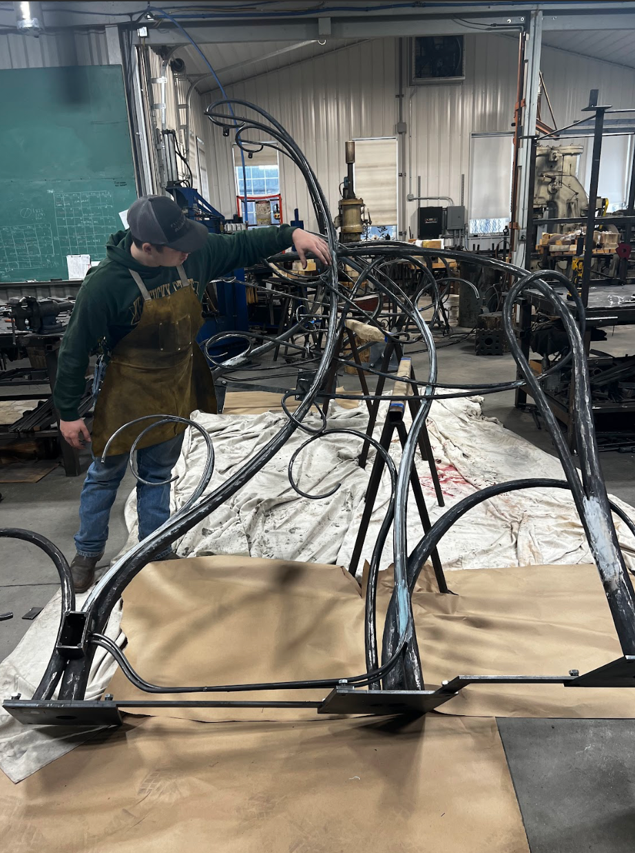 A man is working on a metal sculpture in a workshop.