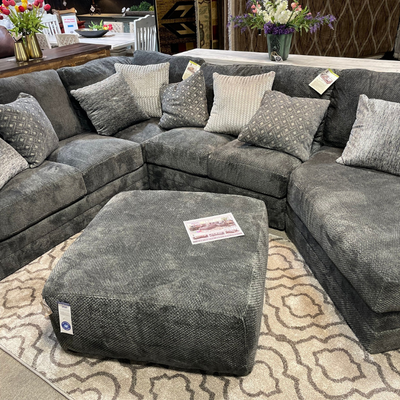Gray modular sectional sofa with matching ottoman and patterned rug in a furniture showroom