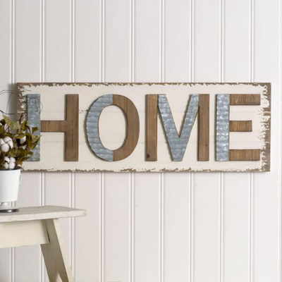 Rustic wooden “HOME” wall sign on white paneled wall beside a small table with flowers