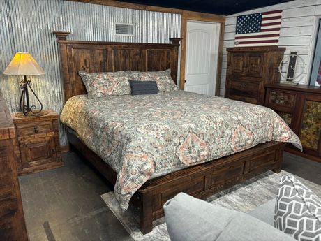 Rustic bedroom with wooden bed, floral bedding, bedside lamps, and an American flag on the wall.