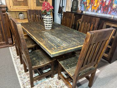 Rustic wooden dining table and chairs in a kitchen, with a vase of red flowers on top