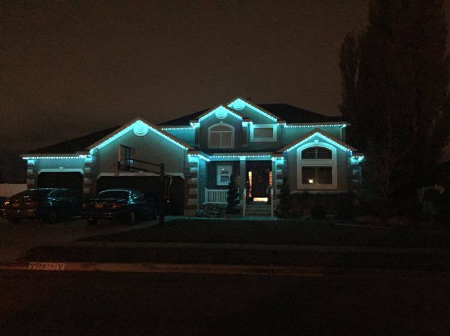 A house that is lit up at night with permanent lighting and cars parked in front of it