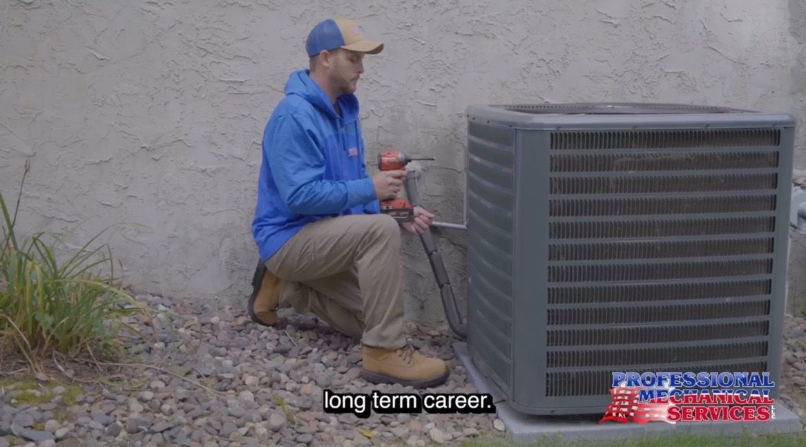 Furnace in a utility room, metal and gray, against a white wall and a gray floor.