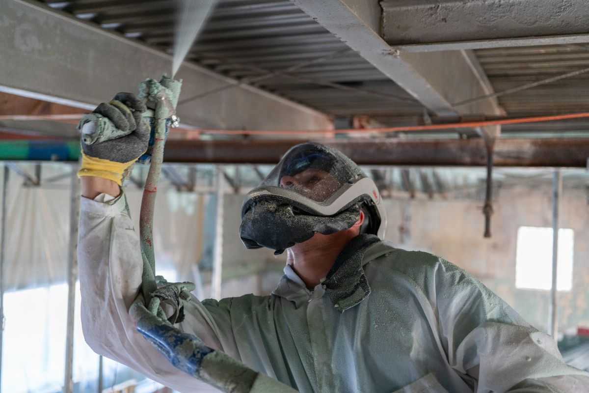 Hands wiring a red electrical outlet in a dark gray wall, using pliers.