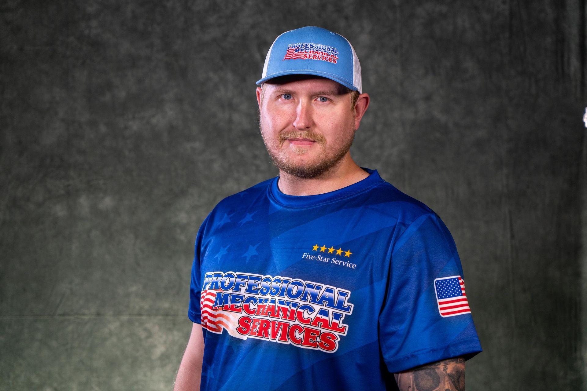A man wearing a hat and sunglasses is standing in front of a white wall.