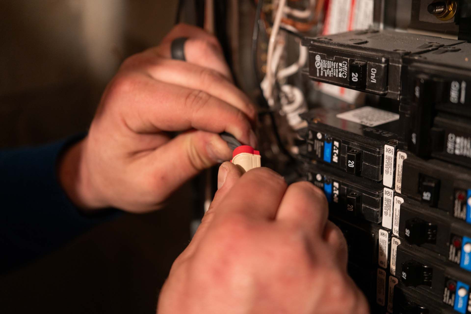 Hands connecting a red wire to an electrical circuit breaker panel