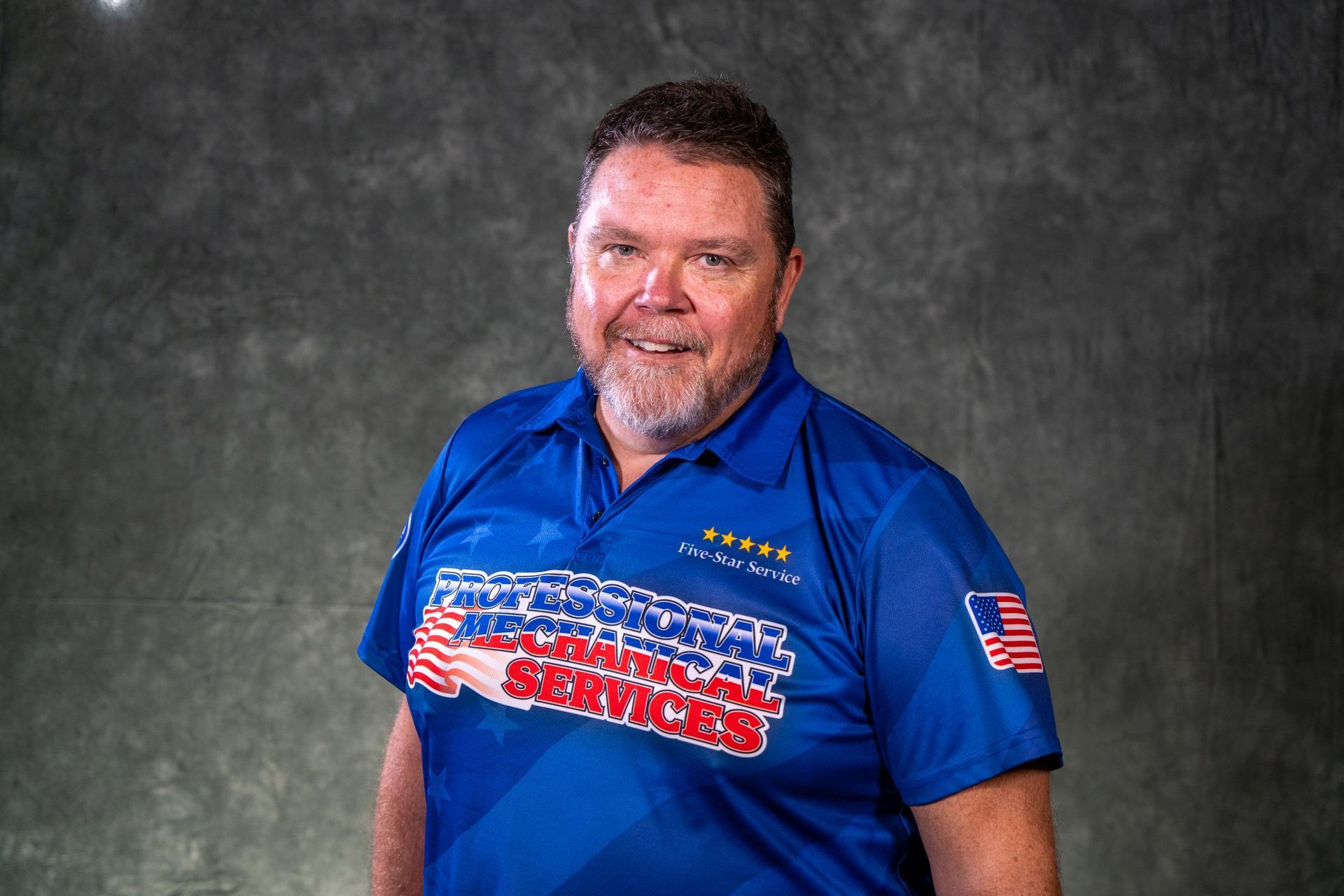 A man with a beard is wearing a black shirt and smiling.