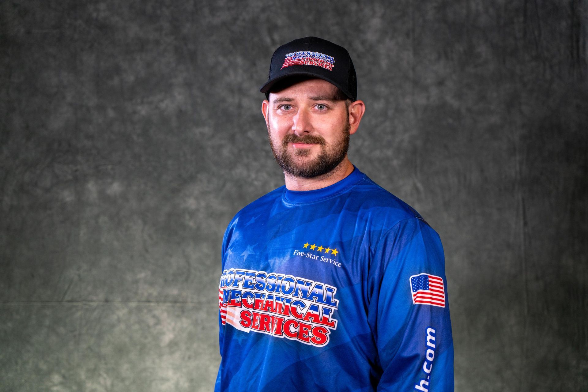 A man with a mustache is wearing a black polo shirt and a hat.