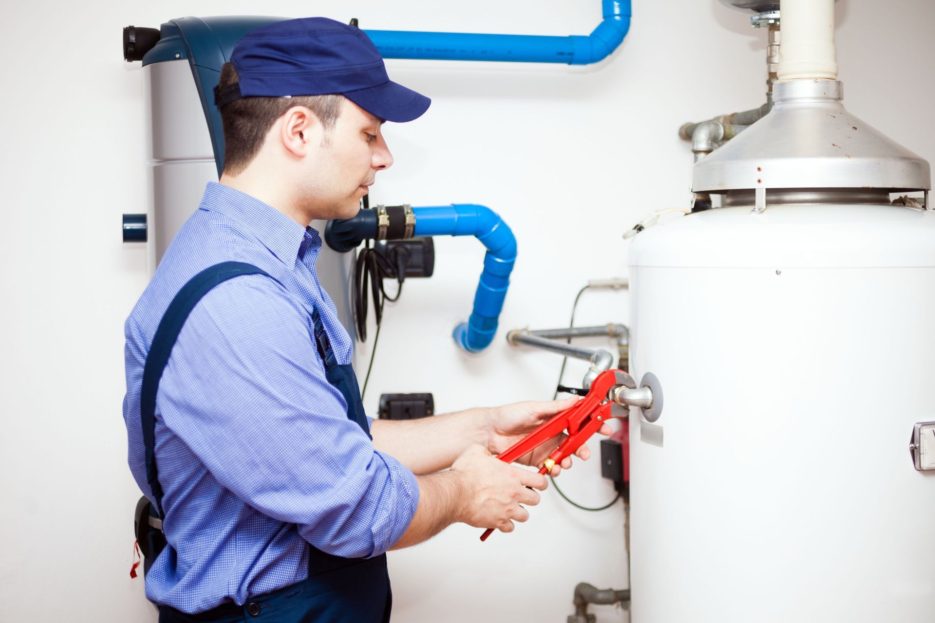 Plumber using red wrench to repair white water heater with blue pipes in a utility room