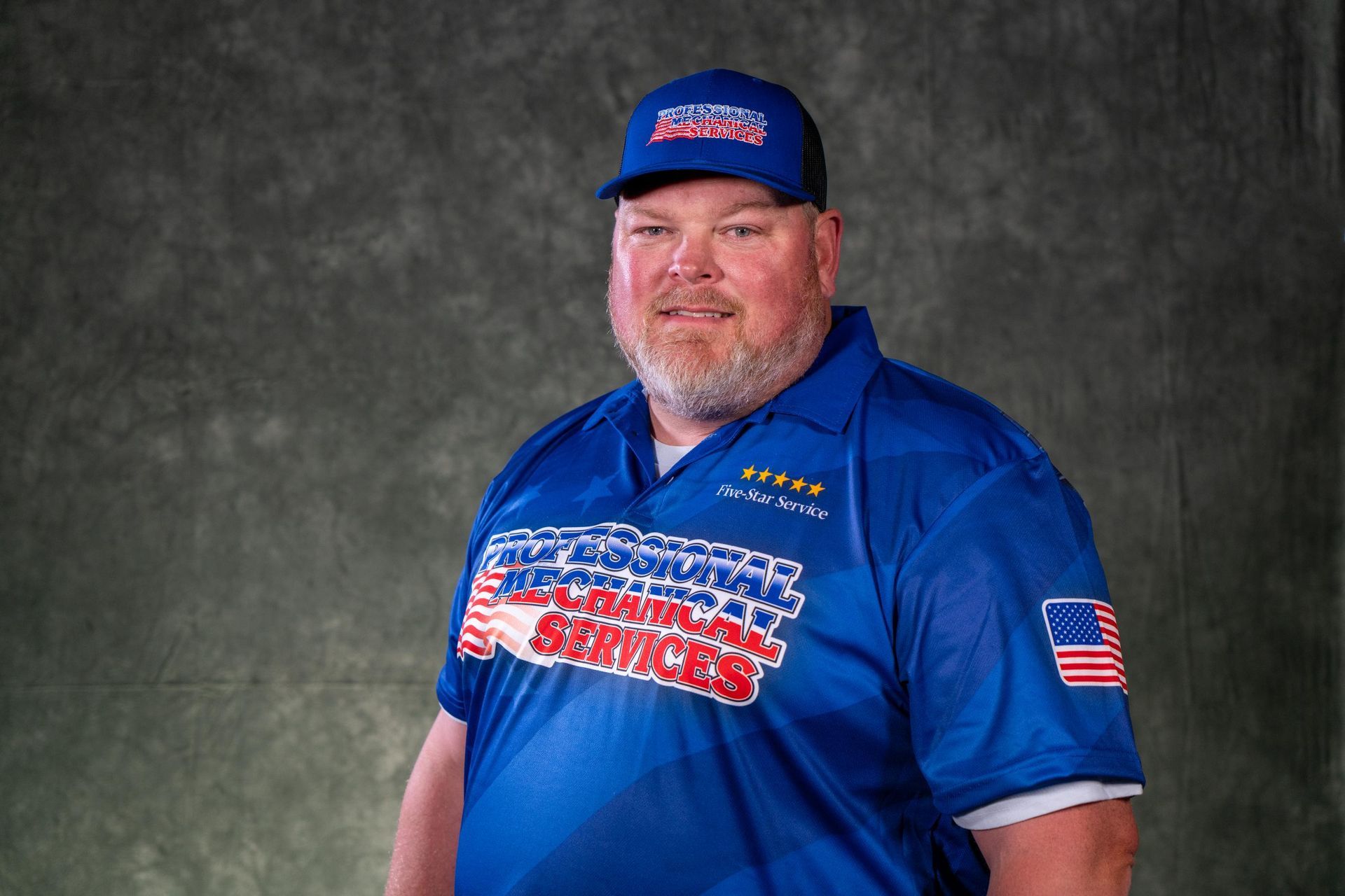A man wearing a hat and sunglasses is standing in front of a white wall.