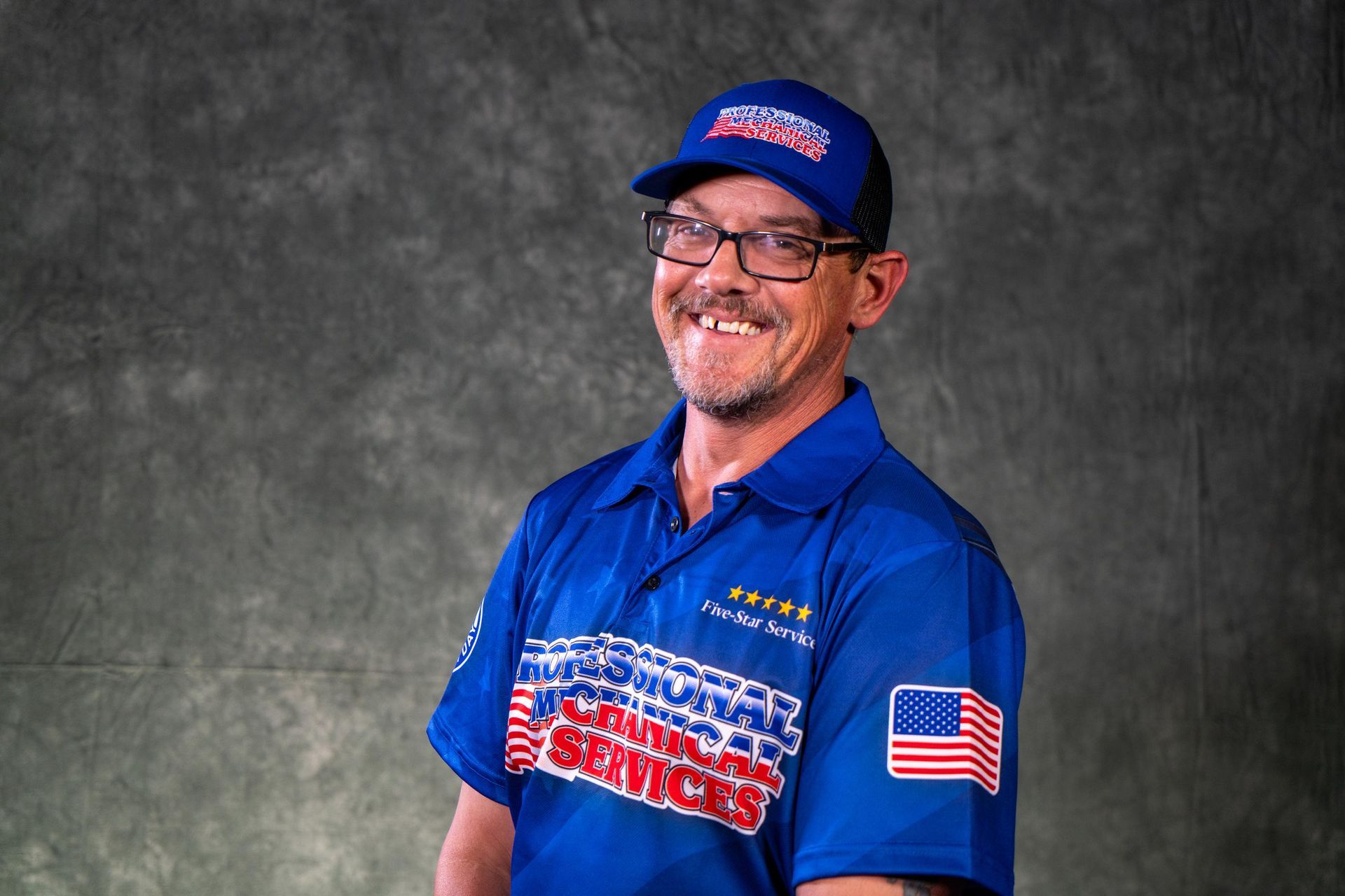 A man wearing a hat and glasses is smiling for the camera.