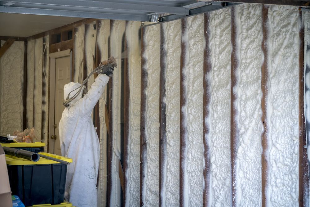Worker installing insulation inside a wall cavity, using spray foam in a partially finished room.