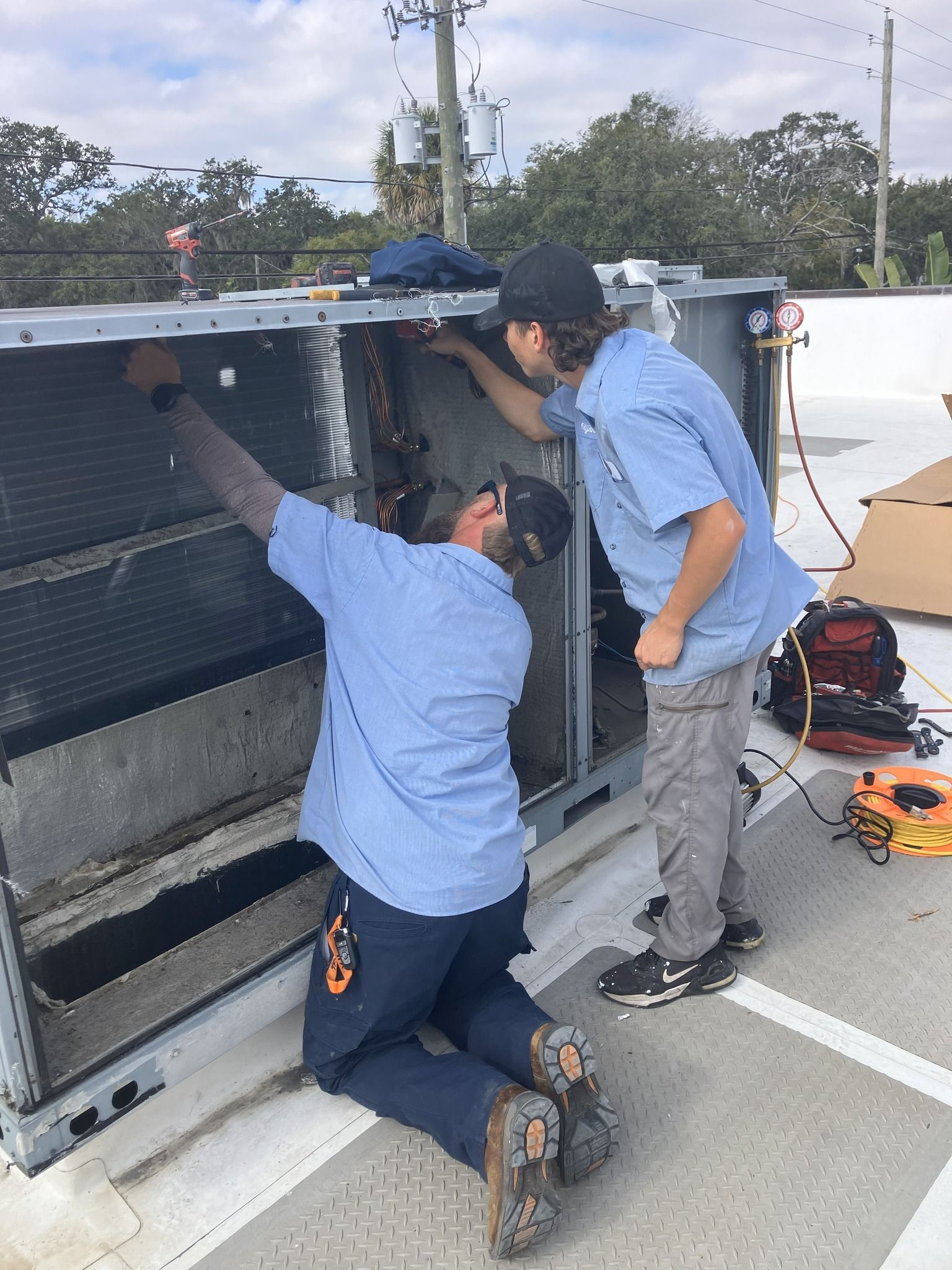 Two HVAC technicians working on rooftop unit. One kneels, the other stands.