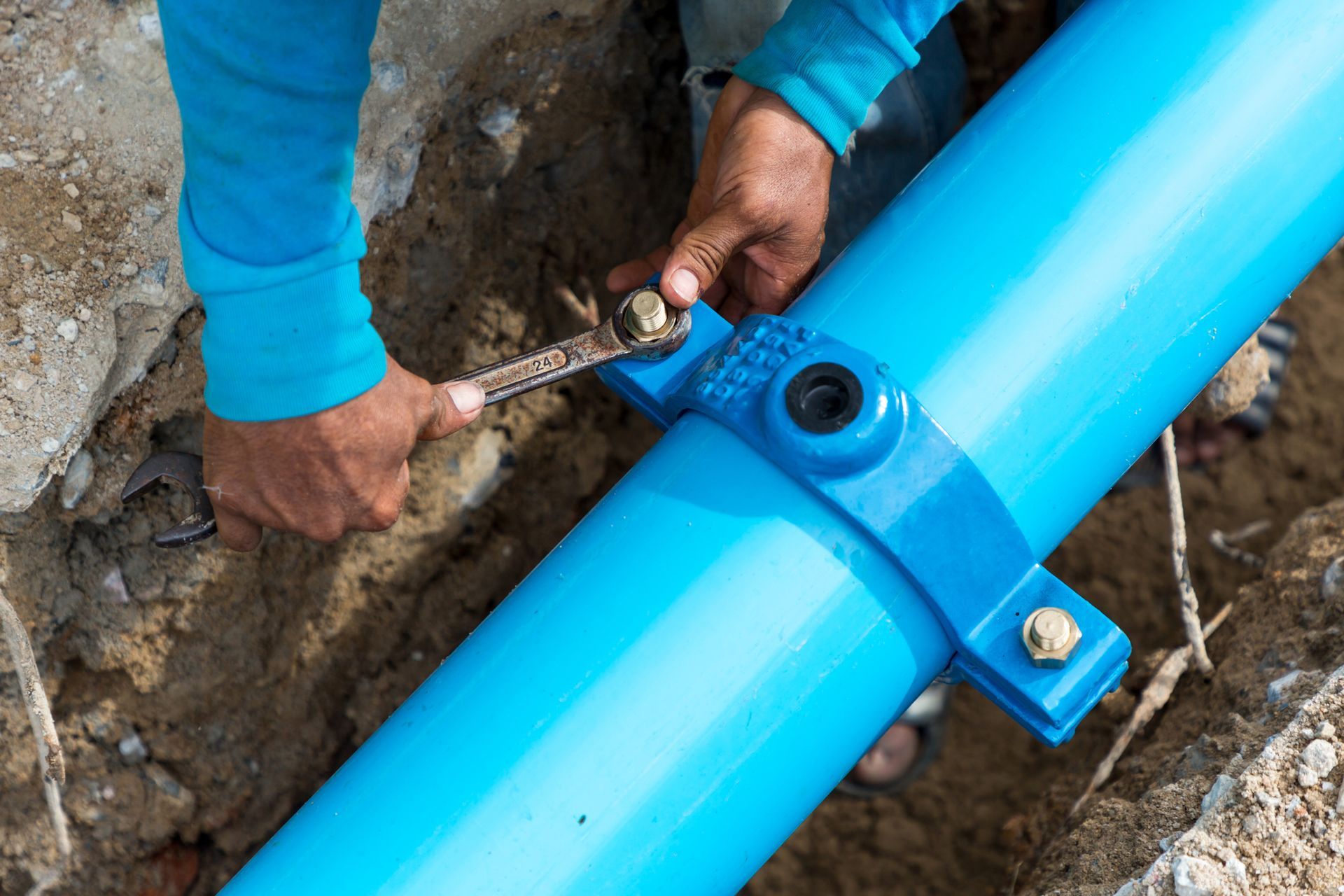 A man is fixing a blue pipe with a wrench.