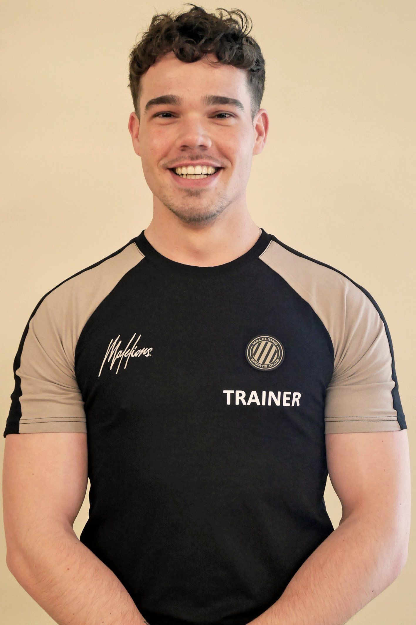 Een man draagt ​​een zwart shirt met de tekst trainer erop