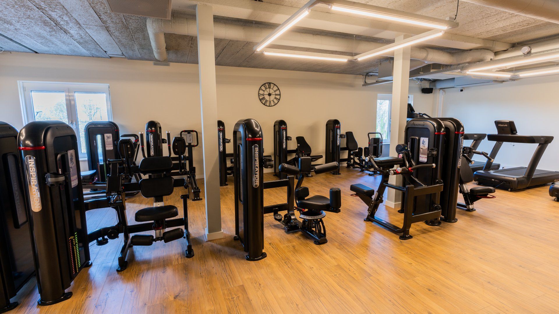 Een sportschool vol met veel fitnessapparatuur en een klok aan de muur.