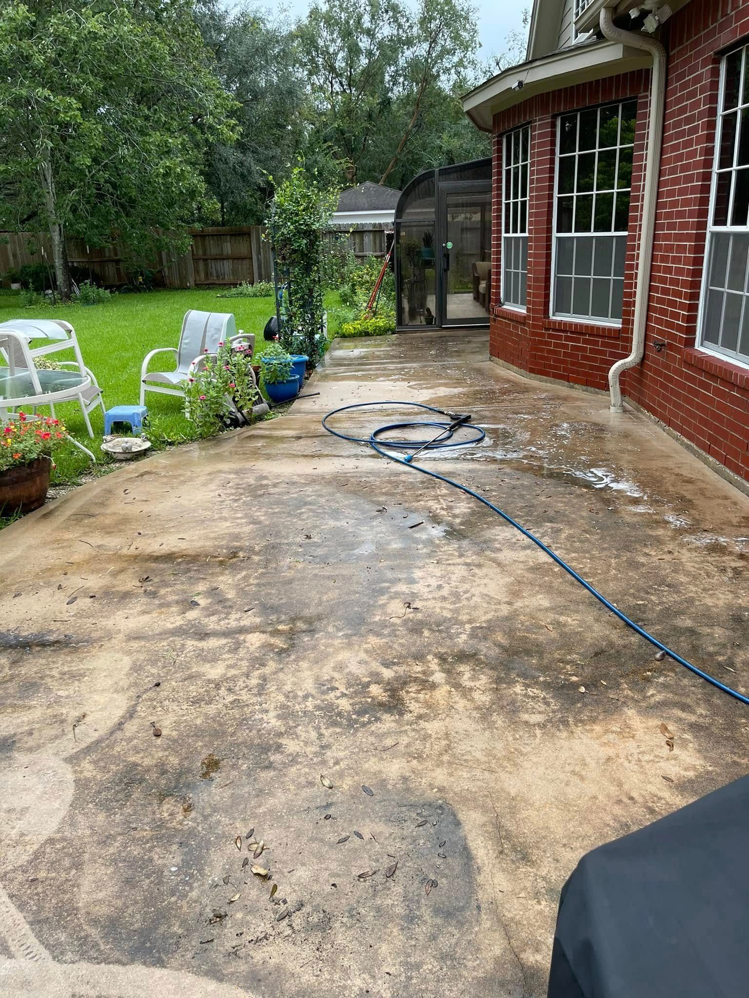 Concrete patio with a hose, next to a red brick house and lawn.