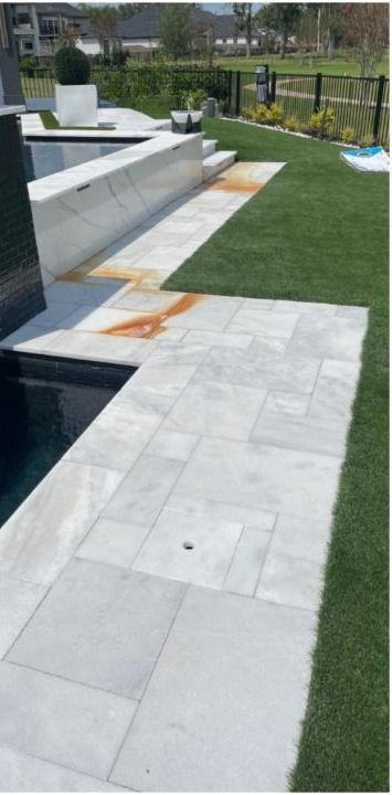 A white tile walkway leading to a pool in a backyard.