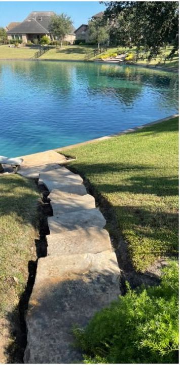 A stone walkway leading to a lake with a house in the background.