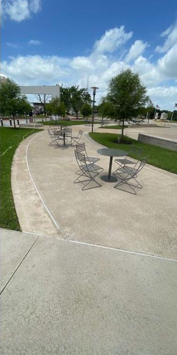 A row of tables and chairs in a park on a sunny day.