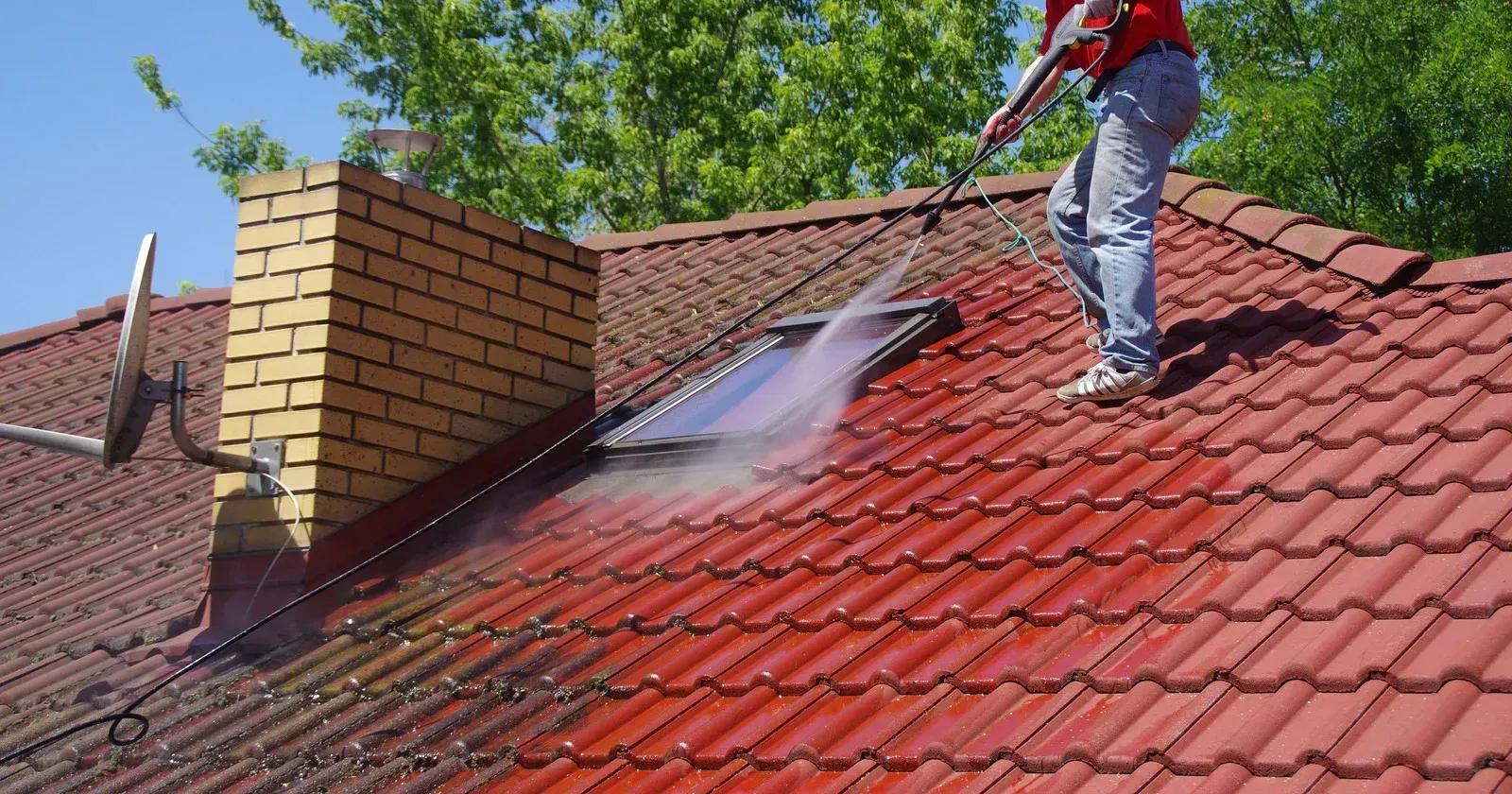 A man is cleaning the roof of a house with a high pressure washer.